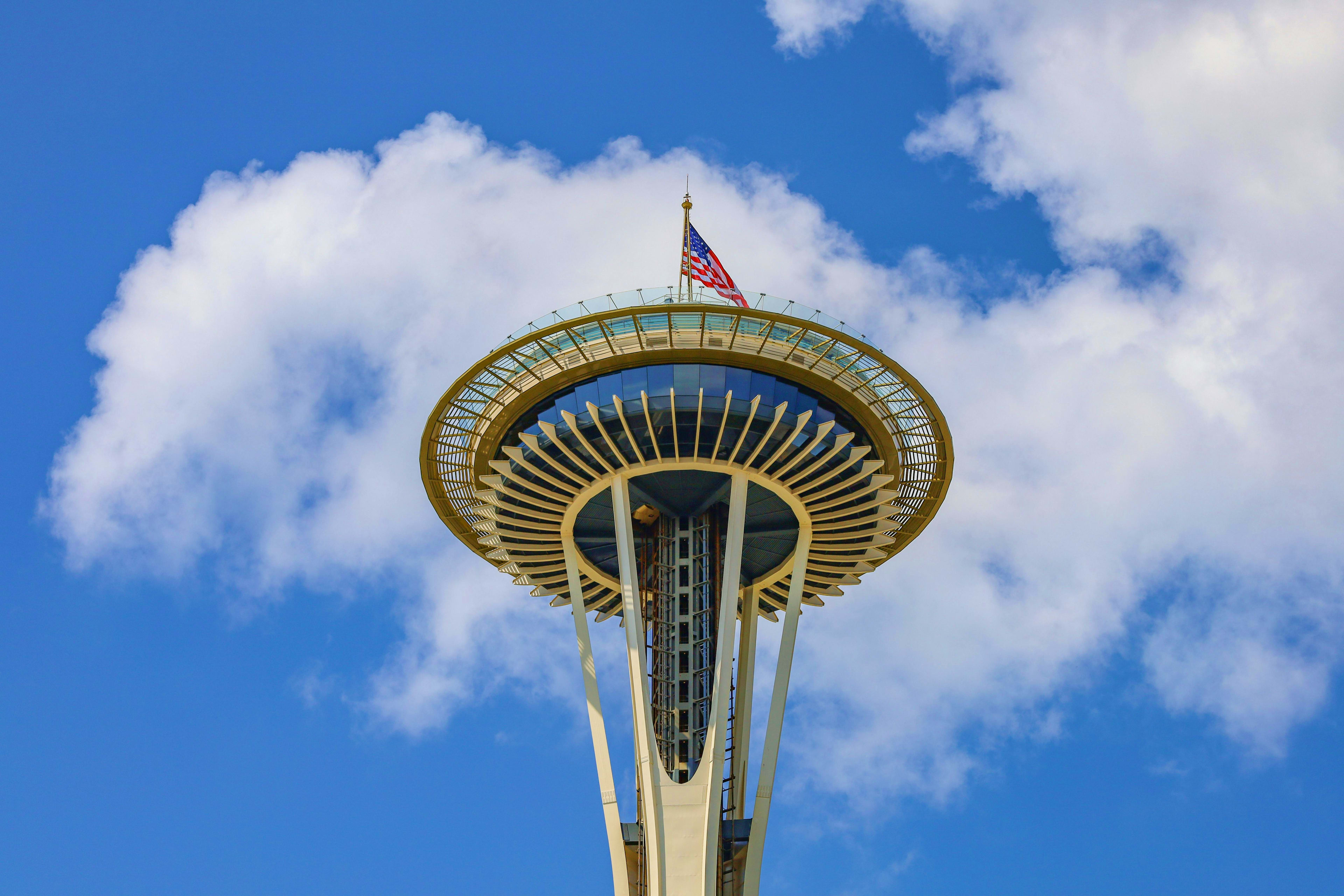 Space Needle observation tower in Seattle with American flag flying from top against blue sky with white clouds